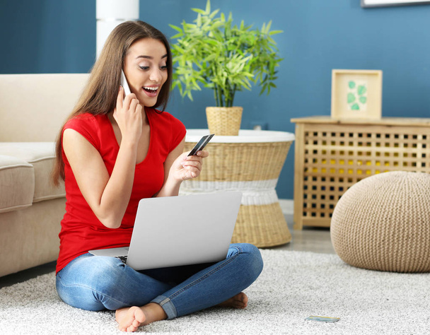 Молодая женщина с ноутбуком и кредитной картой разговаривает по мобильному телефону дома. Интернет-магазины
 - Фото, изображение