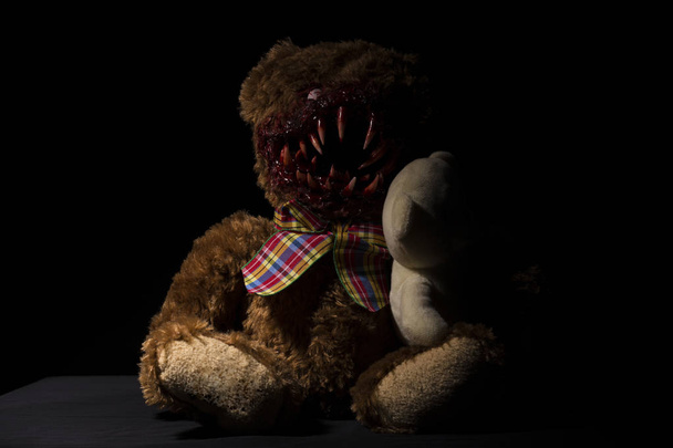um urso terrível com enormes presas no sangue em um fundo preto com um urso bonito em suas mãos
 - Foto, Imagem