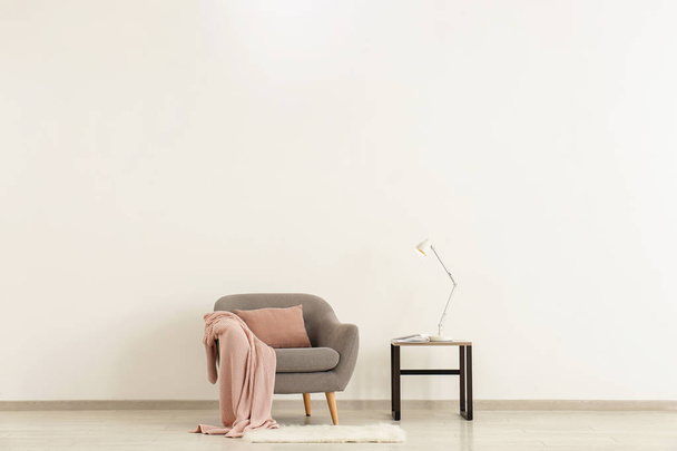 Fauteuil confortable avec table et lampe près du mur de lumière
 - Photo, image