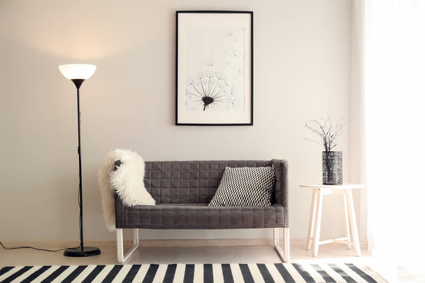 Комфортабельный диван у светлой стены с напольной лампой в интерьере комнаты
 - Фото, изображение