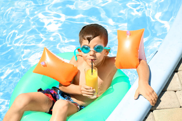 Cute little boy with inflatable ring drinking juice in swimming pool - Photo, Image