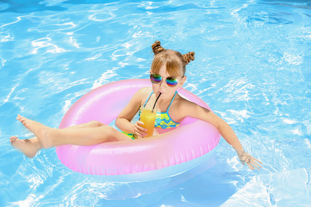 Cute little girl with inflatable ring drinking juice in swimming pool - Foto, Bild
