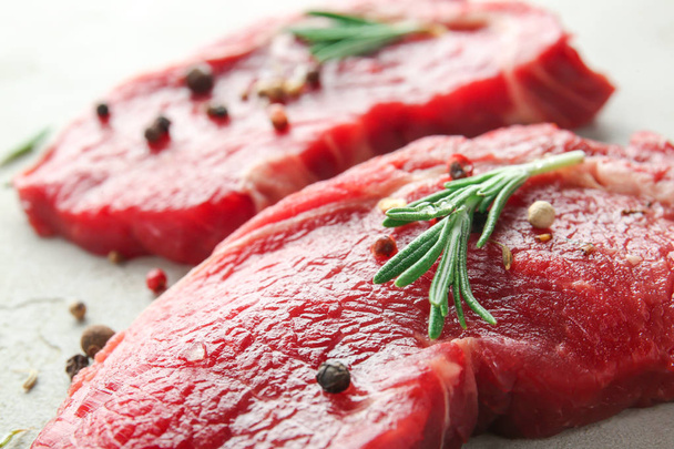 Rauw vlees met specerijen en rozemarijn op een grijze achtergrond, close-up - Foto, afbeelding