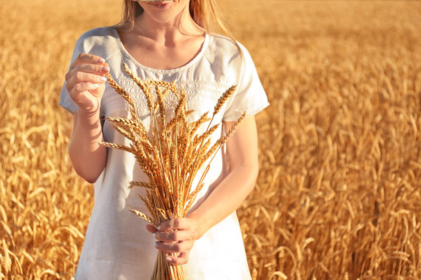 Beautiful woman with wheat spikelets in field on sunny day - 写真・画像