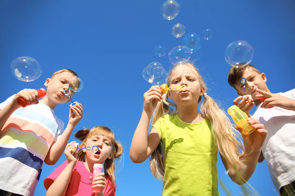 Милые маленькие дети, дующие мыльные пузыри на голубом фоне неба
 - Фото, изображение