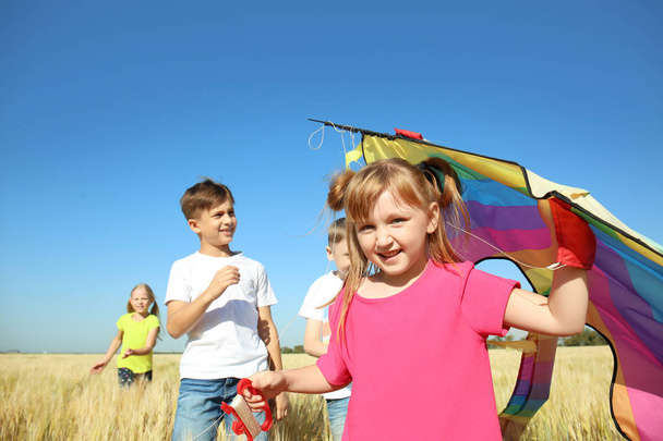 Schattig klein meisje met de vlieger en vrienden in veld op zonnige dag - Foto, afbeelding