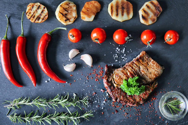 Composição com carne grelhada saborosa, legumes e ervas no prato de ardósia
 - Foto, Imagem