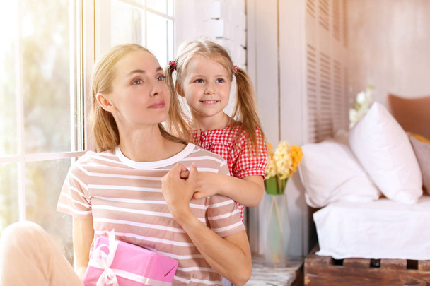 Portrait of cute little girl and her mother with gift box at home - Photo, Image