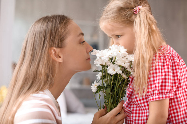 Симпатична маленька дівчинка і її мати нюхають квіти вдома
 - Фото, зображення