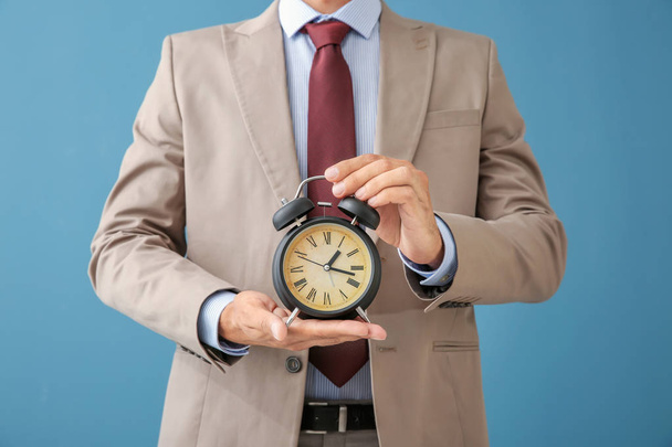 Geschäftsmann hält Wecker auf farbigem Hintergrund. Zeitmanagement-Konzept - Foto, Bild