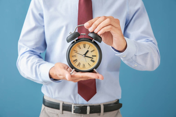 Geschäftsmann hält Wecker auf farbigem Hintergrund. Zeitmanagement-Konzept - Foto, Bild