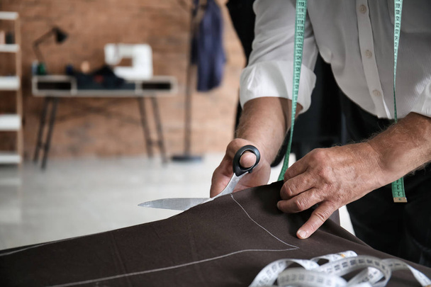 Mature tailor cutting fabric in atelier - Фото, зображення
