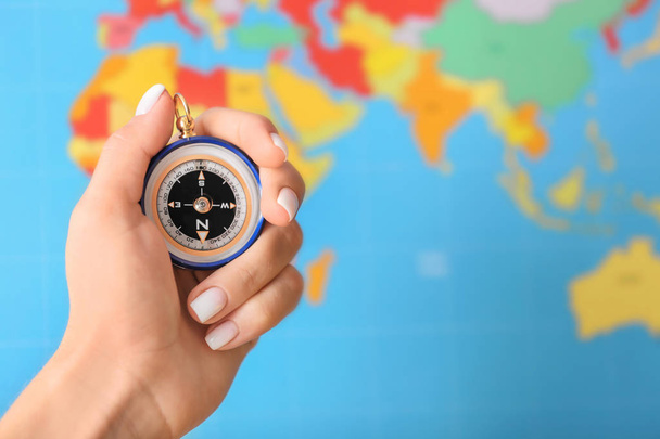 Kobieta trzyma kompas nowoczesne przeciwko mapa świata niewyraźne, zbliżenie - Zdjęcie, obraz