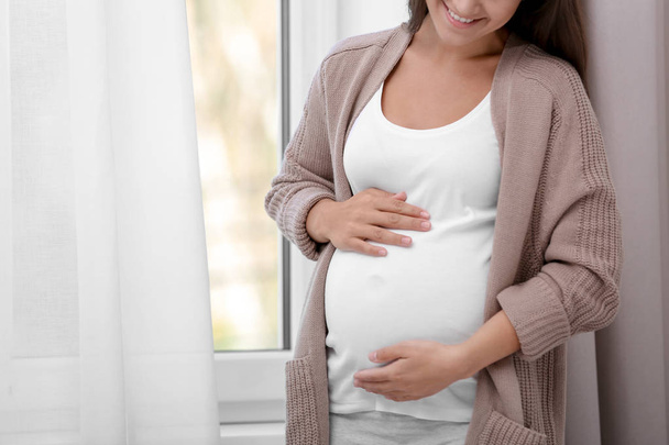 Pregnant woman standing near window at home, closeup - Zdjęcie, obraz
