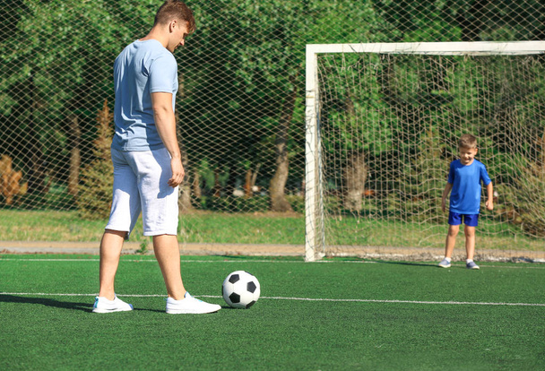Маленький хлопчик зі своїм батьком грає у футбол на футбольному полі
 - Фото, зображення