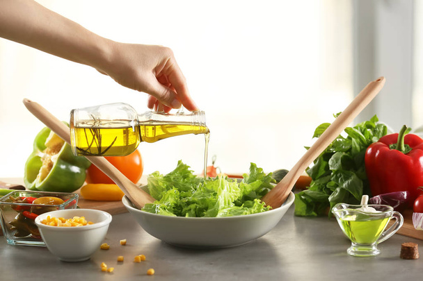 Жінка додає оливкову олію до свіжого овочевого салату на столі
 - Фото, зображення