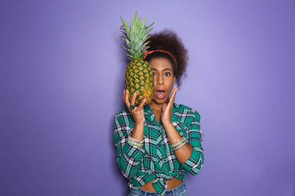 色の背景上にパイナップルと驚かれるアフリカ系アメリカ人女性 - 写真・画像