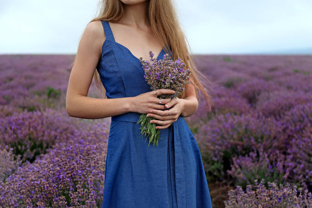 Beautiful young woman with bouquet of lavender in field on summer day - Photo, Image
