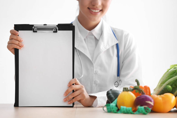 Female nutritionist sitting at table with blank sheet of paper on white background - Photo, Image