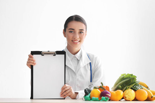Nutricionista sentada a la mesa con hoja de papel en blanco sobre fondo blanco
 - Foto, imagen