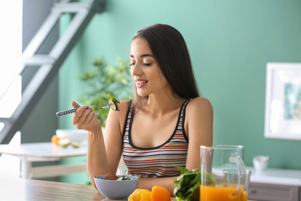 Young woman eating healthy salad with vegetables in kitchen - Фото, зображення