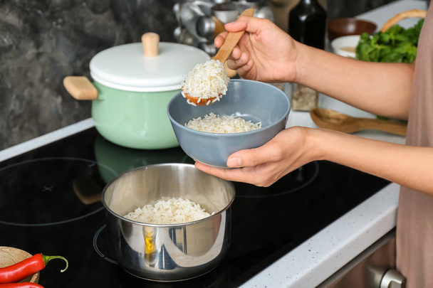 Woman putting freshly cooked rice into bowl in kitchen - Foto, Bild