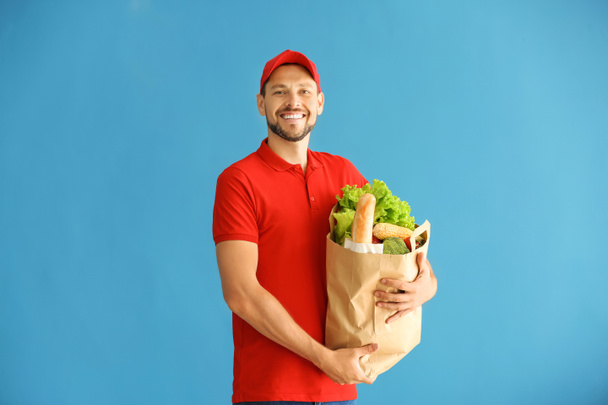 Mann hält Papiertüte mit frischen Produkten auf farbigem Hintergrund. Essenslieferdienst - Foto, Bild