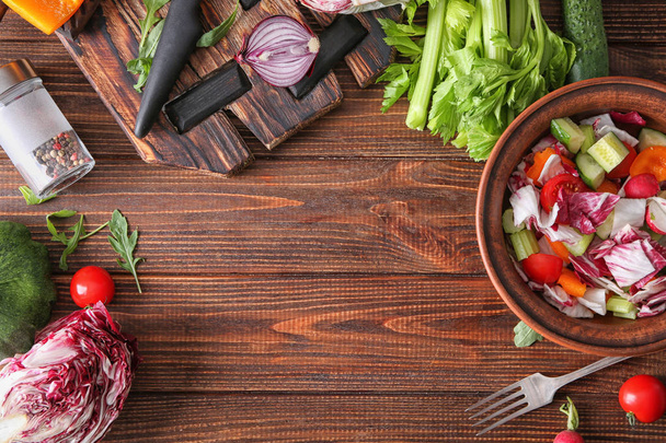 Kom met lekkere groente salade en ingrediënten op houten tafel - Foto, afbeelding