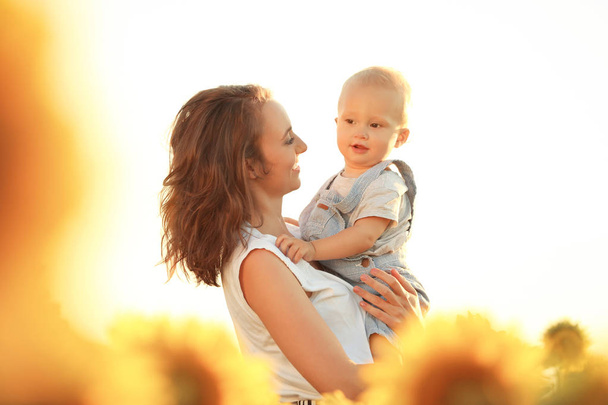 Mulher bonita com seu filho no campo de girassol no dia ensolarado
 - Foto, Imagem