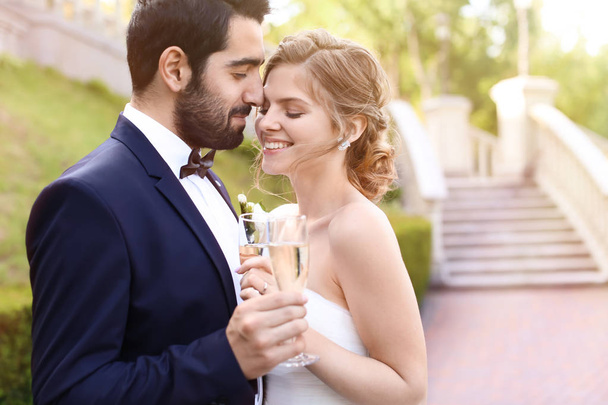 Счастливая свадебная пара с бокалами шампанского на открытом воздухе
 - Фото, изображение