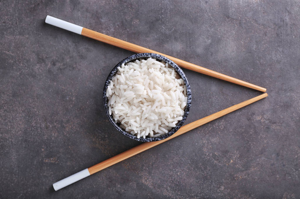 Μπολ με βρασμένο άσπρο ρύζι και chopsticks σε γκρι φόντο με υφή - Φωτογραφία, εικόνα
