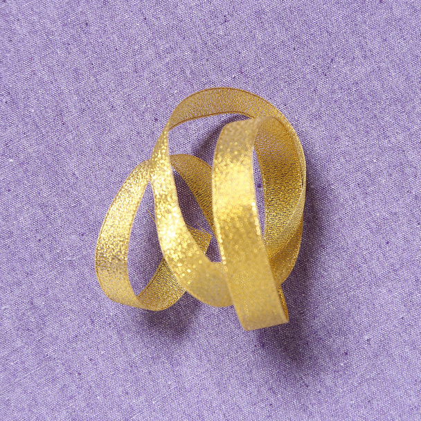 Kudrnatá zlatou stuhou na pozadí fialové látky - Fotografie, Obrázek