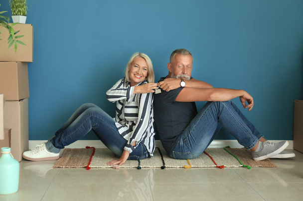 Mature couple with key sitting on floor near boxes indoors. Moving into new house - Photo, Image