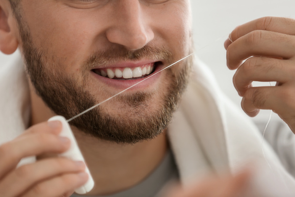Молодой человек чистит зубы нитью, крупным планом
 - Фото, изображение