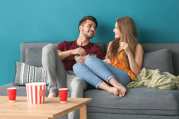 Jeune couple manger du pop-corn tout en regardant la télévision sur le canapé à la maison
 - Photo, image