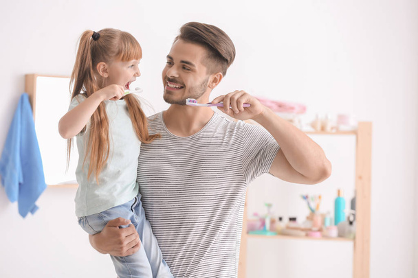 Маленька дівчинка і її батько чистять зуби у ванній
 - Фото, зображення