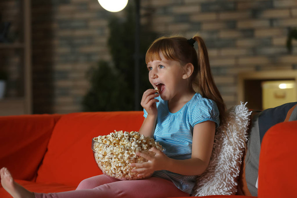 Kislány pattogatott kukoricát eszik este kanapén tévénézés közben - Fotó, kép
