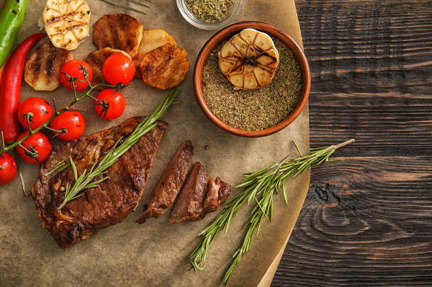 Tasty grilled meat with vegetables, spices and herbs on wooden table - Photo, Image