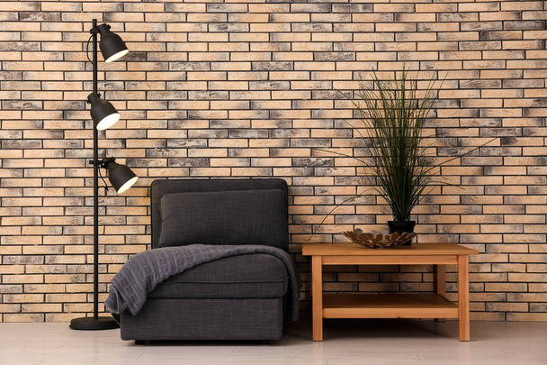Interior da sala de estar com elegante poltrona confortável perto da parede de tijolo
 - Foto, Imagem