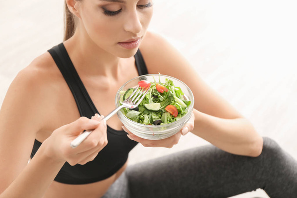 Młoda kobieta sportowy w domu jedzenie sałatką ze świeżych warzyw - Zdjęcie, obraz