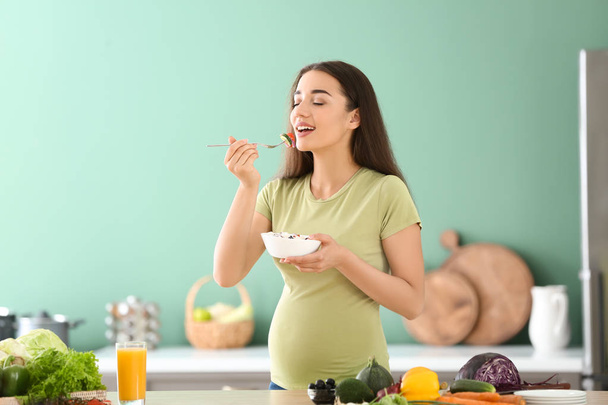 Young pregnant woman eating fresh vegetable salad in kitchen - Foto, Imagem