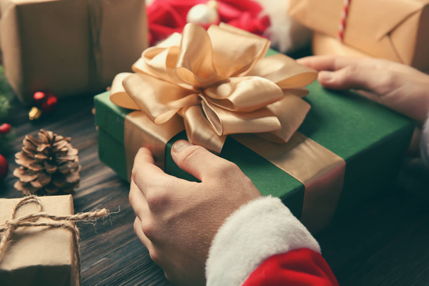 Noel Baba hediye kutusu ahşap masa üzerinde tutan - Fotoğraf, Görsel