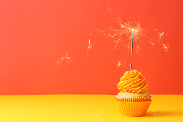 Delicious birthday cupcake with sparkler on color background - Photo, Image