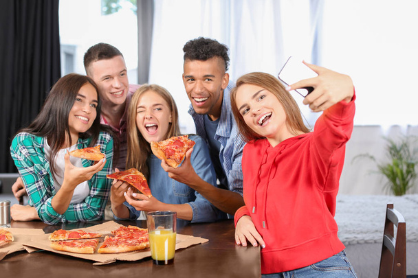 Молодые люди делают селфи на вечеринке с вкусной пиццей в помещении
 - Фото, изображение