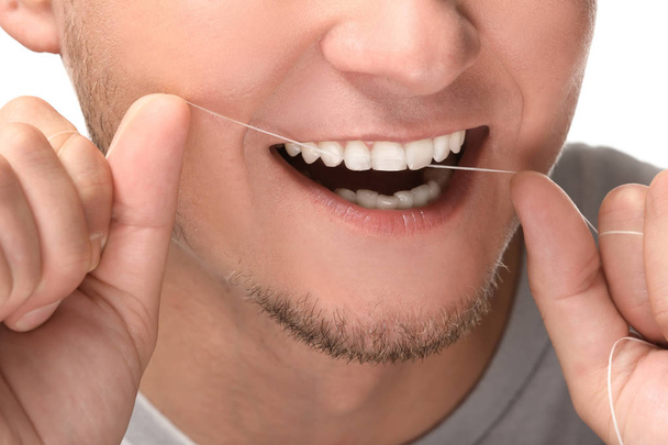 Man flossen zijn tanden op witte achtergrond, close-up - Foto, afbeelding