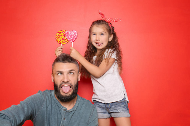 Funny portrait of father and his little daughter with lollipops on color background - Photo, Image