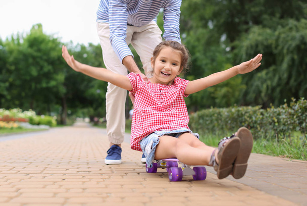 Menina e seu pai brincando com skate ao ar livre
 - Foto, Imagem