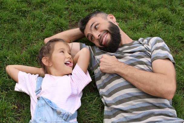 Маленькая девочка и ее отец лежат на зеленой траве на открытом воздухе
 - Фото, изображение