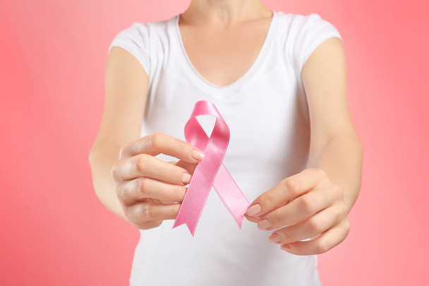 Mulher segurando fita rosa no fundo da cor, close-up. Conceito de consciência do câncer de mama
 - Foto, Imagem