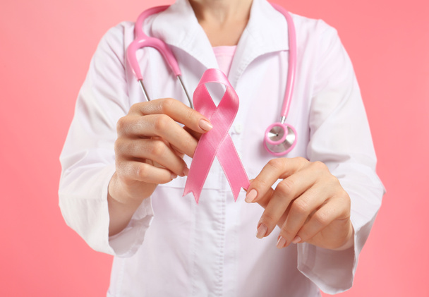 Doctor holding pink ribbon on color background. Breast cancer awareness concept - Foto, Imagen